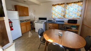 A compact kitchen with wooden cabinets, a white refrigerator, a stove, a microwave, and a dining table with chairs. - Cabin 6 - Reel and Trigger (Tom Township)