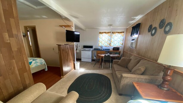 A compact living space with a sofa, a dining table, a kitchen area, and a TV mounted on the wall. - Cabin 6 - Reel and Trigger (Tom Township)