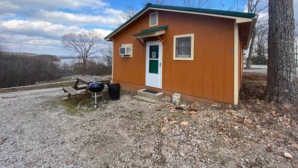 A small wooden cabin with a green door, a window, and a small porch area. - Cabin 8 - Reel and Trigger (Tom Township)