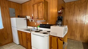 Une cuisine compacte avec des meubles en bois, un réfrigérateur blanc, une cuisinière, un four à micro-ondes et une machine à café.