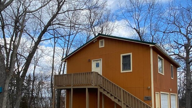 A two-story wooden building with a covered porch and a garage. - Eagle's Nest - Reel and Trigger (Tom Township)