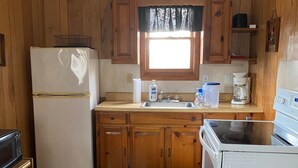 A compact kitchen with wooden cabinets, a refrigerator, a microwave, a sink, and a stove. - Eagle's Nest - Reel and Trigger (Tom Township)