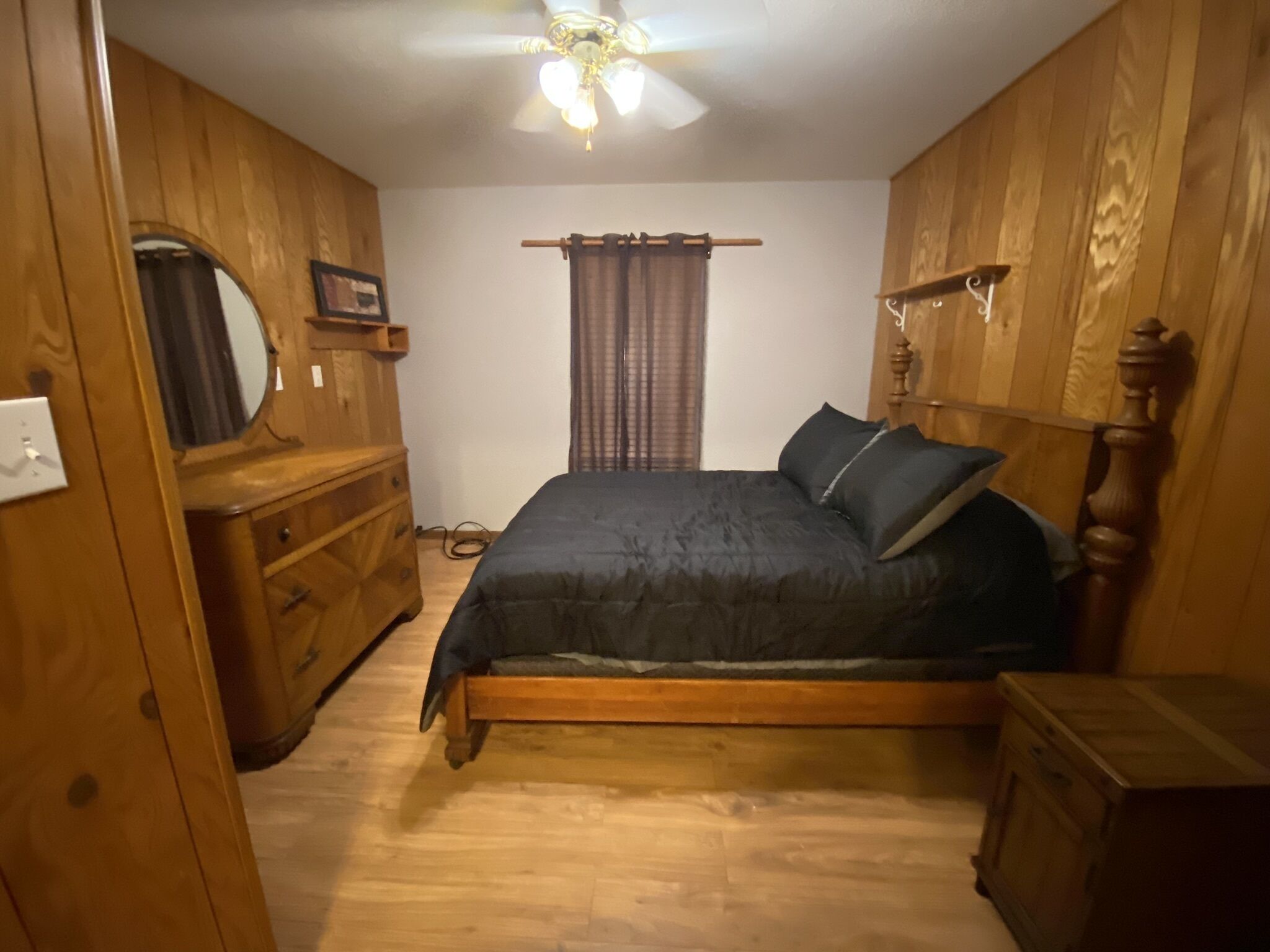 Ein Schlafzimmer mit einem hölzernen Bett, einem Schminktisch, einem Spiegel und einem Deckenventilator.