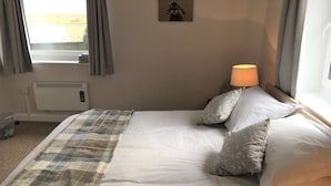 Un letto rifatto con una coperta a quadri, una lampada da comodino e un quadro appeso al muro.