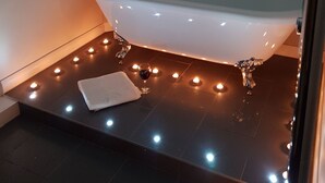 Un bagno moderno con una vasca da bagno freestanding, una decorazione a forma di cuore sulla parete e una fila di candele sul pavimento.