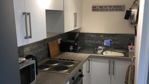 A compact kitchen with white cabinets, a built-in oven, a microwave, a gas stove, and a sink. - Hurricane - 2 bed apartment (Friskney)