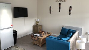 En moderne stue med et fladskærms-tv, en sofa, et sofabord og et lille træskab.