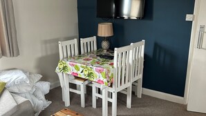 A room with a dining table set for four, a television mounted on the wall, and a wooden coffee table with a document on it. - Spitfire - 2 bedroom apartment (Friskney)