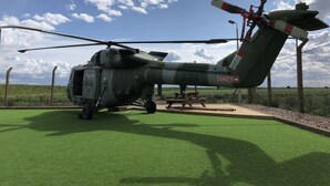 A military helicopter parked on a grassy field with a fence in the background. - Glamping pod helicopter (Friskney)