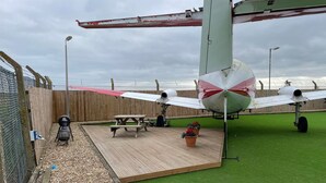 Uma aeronave pequena em exposição, com uma mesa de piquenique e plantas em vasos por perto.
