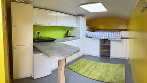 Eine kompakte Küche mit integriertem Kühlschrank, einer kleinen Spüle und einem Wasserkocher auf der Arbeitsfläche.