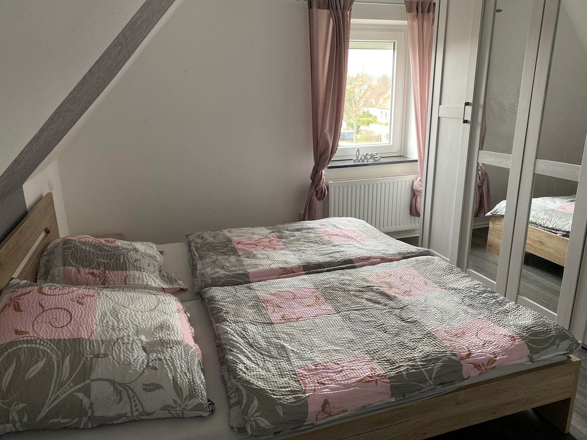 A bedroom with a wooden bed, two pillows, a window with curtains, and a view of the outside.