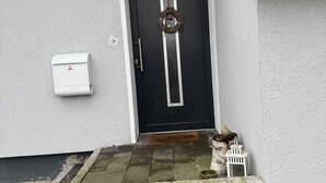 A black door with a wreath, a mailbox, and a small white chair outside a building with a stone step and a tiled roof. - Haus in Ruhiger Lage (Bad Fallingbostel)