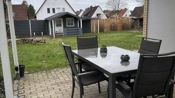 En uteplats med ett bord och stolar, en ljusslinga och utsikt över ett hus i bakgrunden.