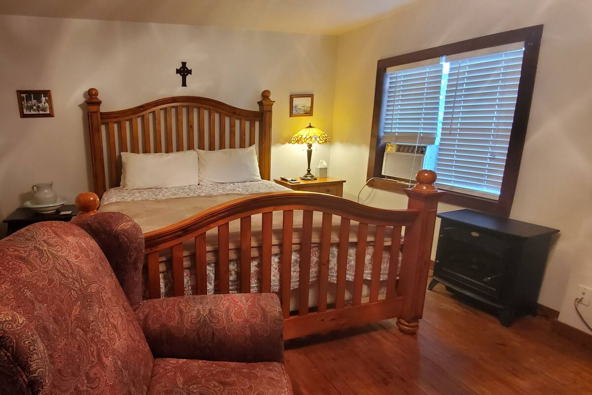 Un dormitorio con una cama de madera, una mesita de noche, una lámpara, un aparador y una ventana con persianas.