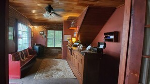 Un interior acogedor con techo de madera, un banco rojo, una zona de cocina con mostrador y una escalera.