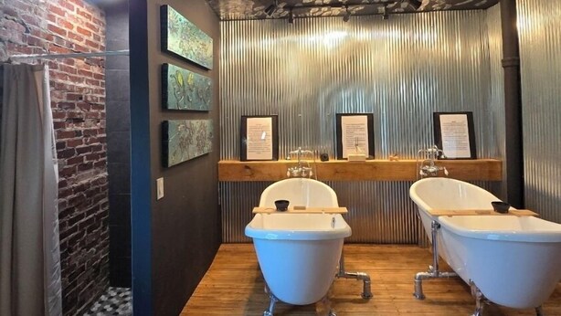 Un baño con dos bañeras blancas tipo pata de león, una pared de ladrillo y un techo decorado con motivos de hojas.