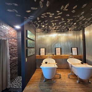 Ein Badezimmer mit zwei weißen Badewannen auf Füßen, einer Ziegelwand und einer Decke mit Blattmustern.