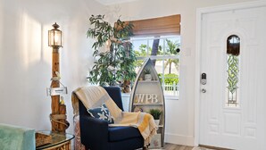 A cozy living room with a blue armchair, a tall lamp, a potted plant, and a decorative shelf.