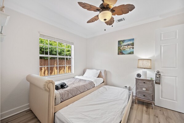 A bedroom with a bed, a nightstand, a ceiling fan, a window, and a door.