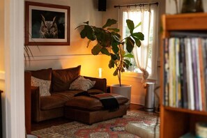 A cozy living room with a brown leather sofa, a potted plant, a bookshelf, and a framed picture on the wall.