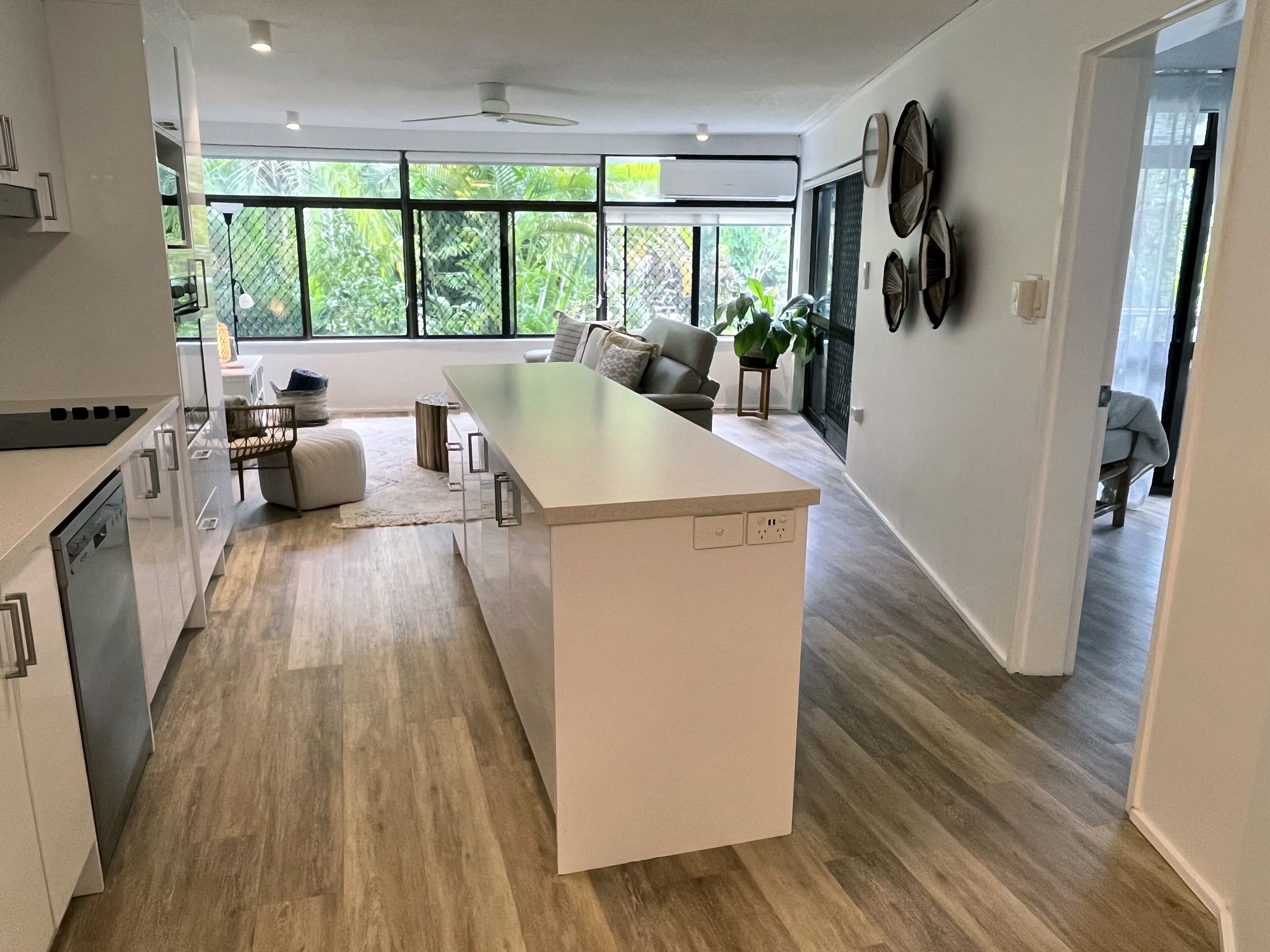 A modern kitchen with a central island, large windows, and a view of greenery outside.