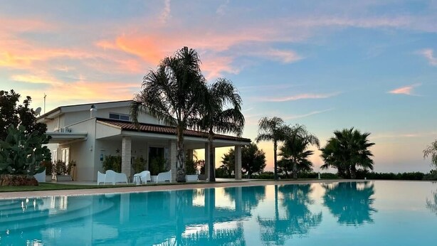Un complexe hôtelier moderne doté d’une piscine, de palmiers et offrant une vue sur un ciel au coucher du soleil.