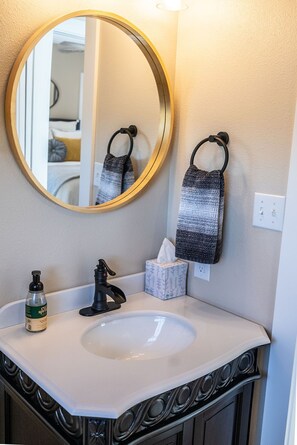 A bathroom with a round mirror, a sink, a bottle of hand soap, a towel, and a tissue box. - The Eagle's Nest:  A Charming Oasis Minutes from Decatur Square (Decatur)