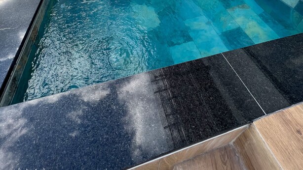 Een dakterras zwembad met oneindige horizon, gevuld met helderblauw water, omgeven door glazen relingen en moderne architectuur.