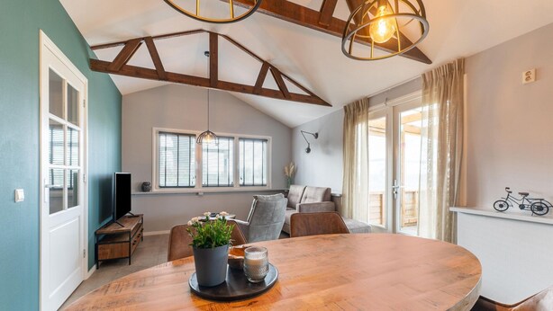 A spacious living area with a wooden dining table, comfortable seating, and a large window with blinds. - Charming House With Garden (Hellendoorn)