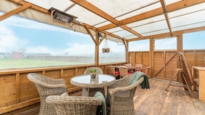 A covered outdoor area with wooden flooring, wicker furniture, and a table with chairs. - Charming House With Garden (Hellendoorn)