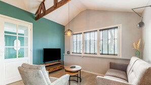 A living room with a TV, two sofas, a coffee table, and a window with blinds. - Charming House With Garden (Hellendoorn)