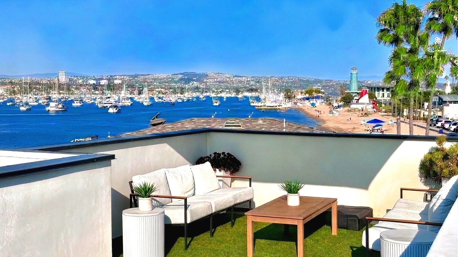 Une terrasse sur le toit offrant une vue sur un port de plaisance et une plage, aménagée avec un canapé, une table et des plantes en pot.