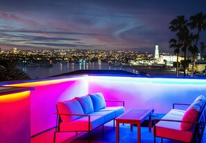 An outdoor pool area with seating and a view of a cityscape at night.
