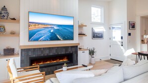 A living room with a fireplace, a large TV mounted above it, and a coastal view.