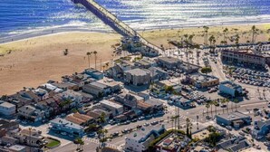 An aerial view of a coastal town with a pier extending into the ocean, a beach, and a dense cluster of buildings.