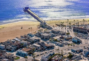 Vista aérea de un pueblo costero con un muelle que se adentra en el océano, una playa y un grupo denso de edificios.