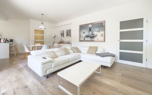 Uma sala de estar moderna com um sofá branco, uma mesa de centro e uma área de jantar com cadeiras e uma mesa.