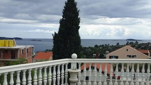 Un balcon doté d’une balustrade blanche, offrant une vue sur la côte, avec des bâtiments et un grand arbre.