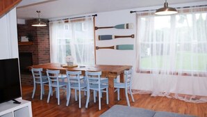 Un comedor con una mesa de madera y seis sillas, un televisor sobre un soporte blanco y un sofá gris.