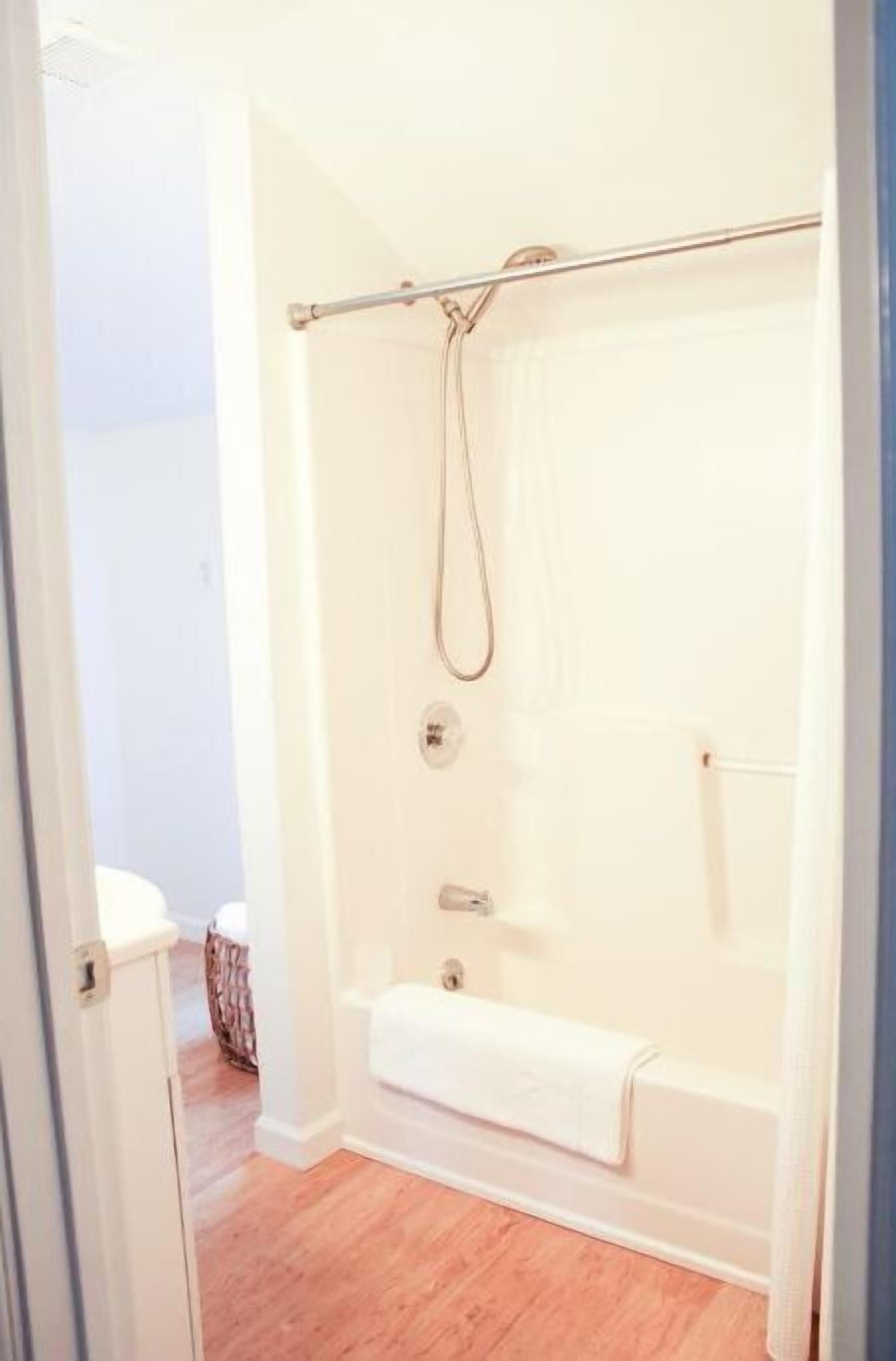 A bathroom with a glass-enclosed shower, a white bathtub, and a wooden floor.