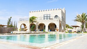 Um edifício de pedra com janelas em arco e uma piscina em frente.