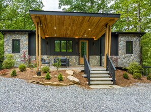 Une maison moderne avec une façade en pierre, une terrasse en bois et un escalier en pierre menant à la porte d’entrée.