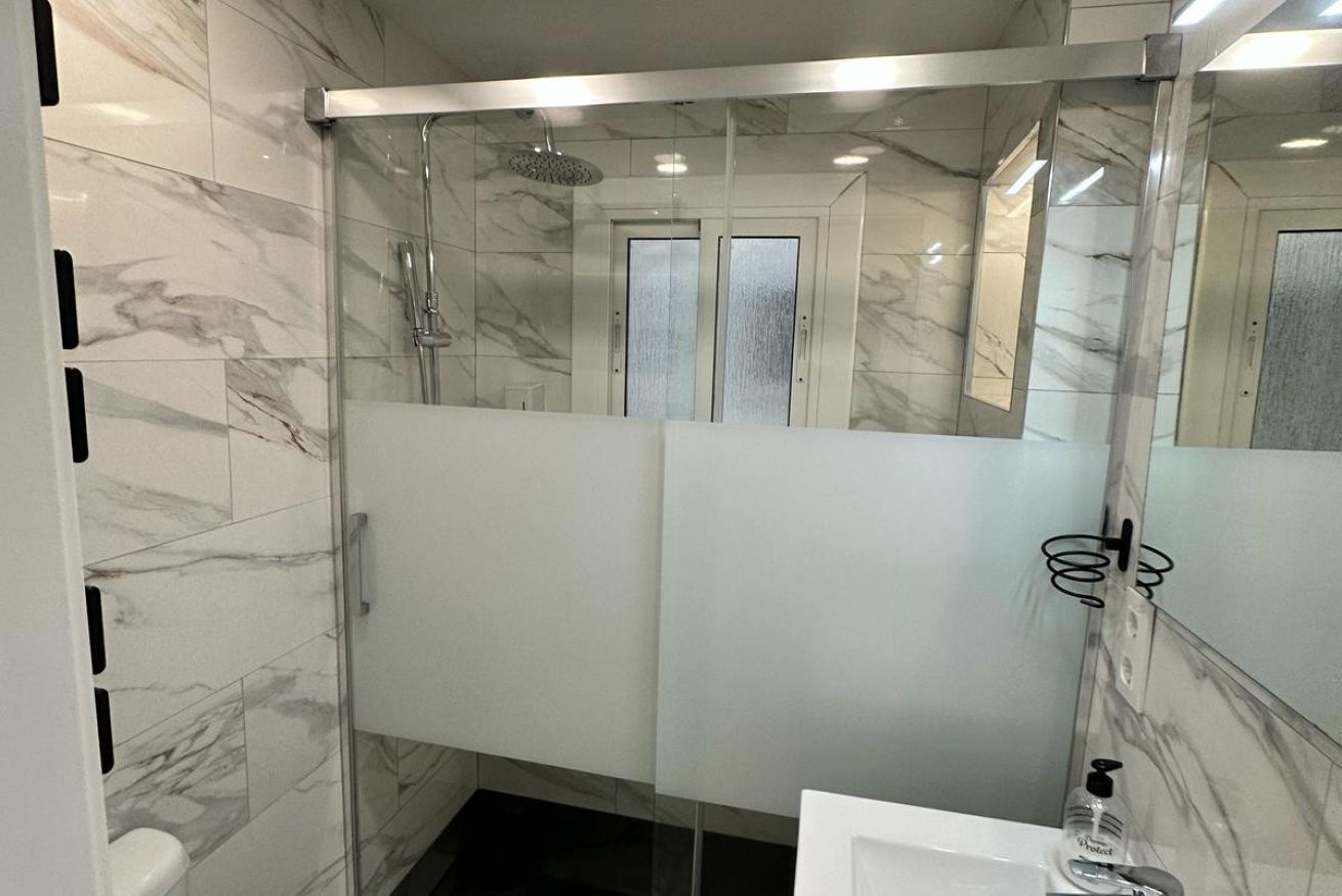 Un baño moderno con ducha de vidrio, azulejos de mármol y un espejo grande.