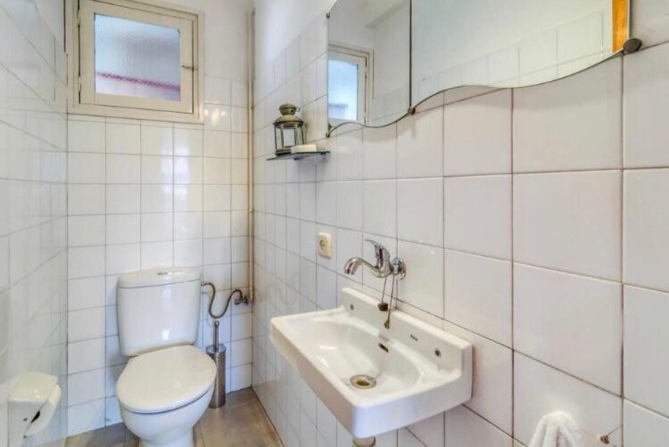 Un bagno con piastrelle bianche, un water, un lavandino e una piccola finestra.