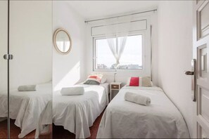 Une chambre d’hôtel avec deux lits, une fenêtre avec des rideaux légers, une table de chevet, un miroir et une vue sur la ville.