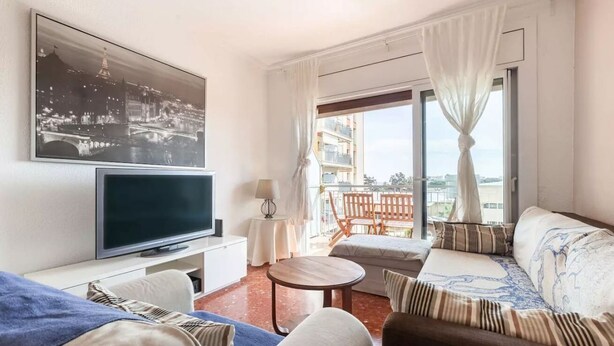 Una sala de estar moderna con televisor de pantalla plana, un sofá, una mesa de centro y un balcón con vistas.