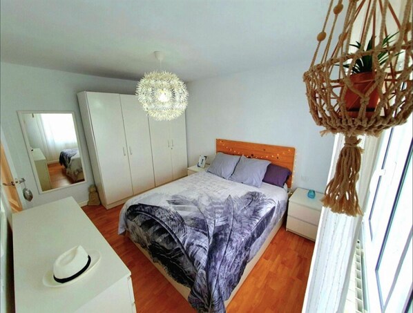 A bedroom with a bed, a wardrobe, a desk, and a hanging macrame light fixture.