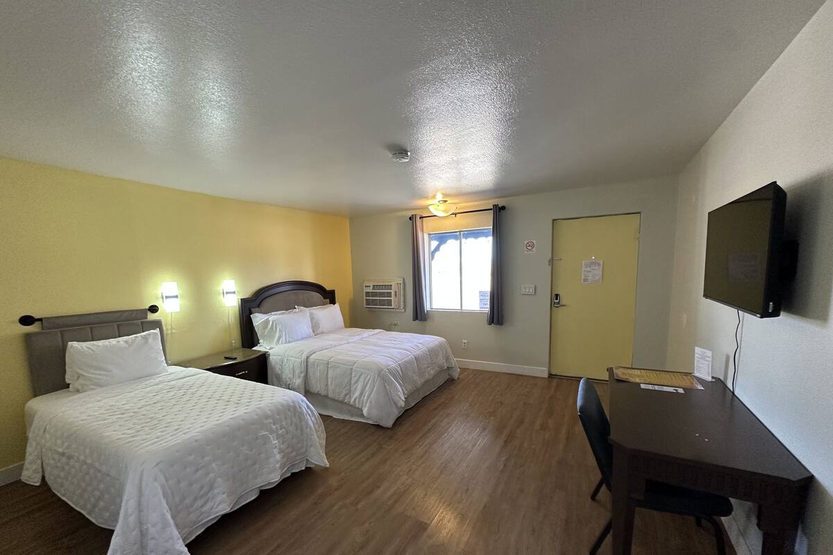 A room with two beds, a desk, a chair, a TV, and a window with curtains.