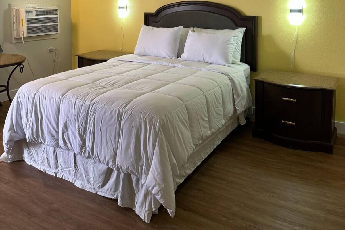 A bedroom with a large bed, two bedside tables, a wall-mounted air conditioner, and two wall-mounted lights.